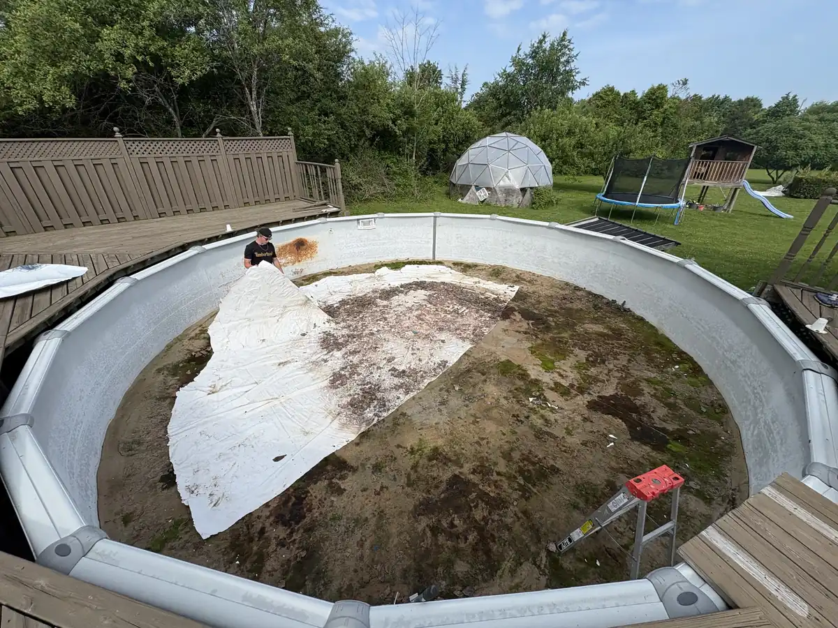 Old above ground liner being pulled out, showing the sand base