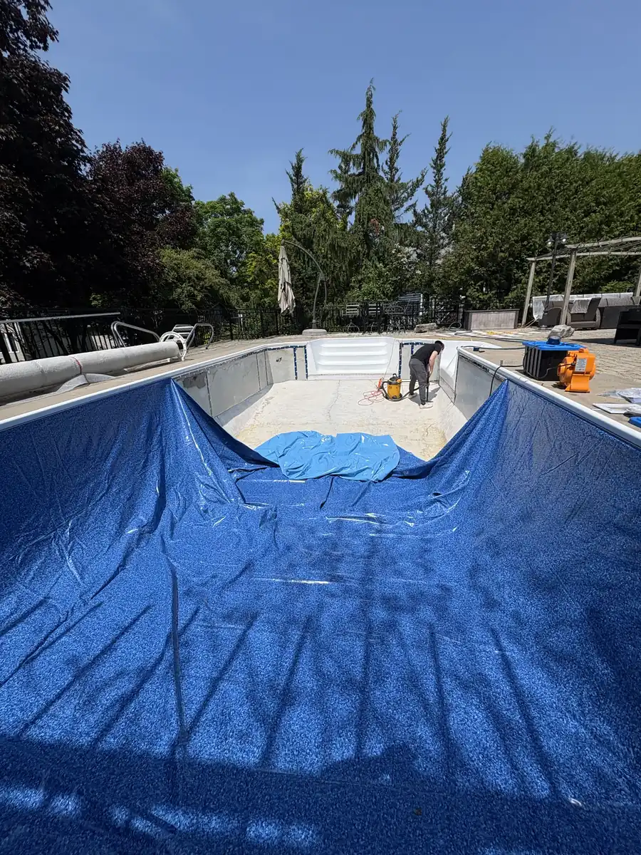 New blue vinyl liner being set in a drained rectangular pool
