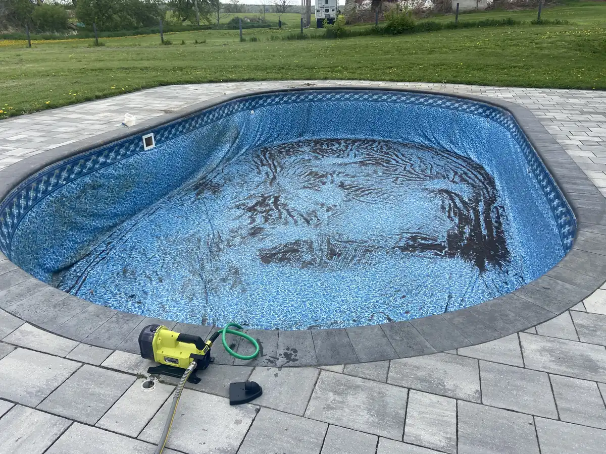 Oval pool on a rural property, nearly empty with dirty, stained water